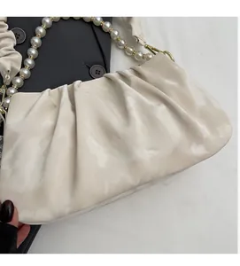 Detail of cream pleated cloud bag featuring pearl beaded strap and soft fabric texture