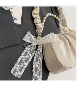 Detail of cream pleated cloud bag featuring pearl chain strap and lace bow accent