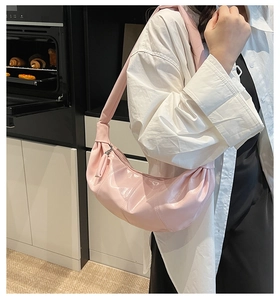 Pink patent leather half-moon bag worn by model in a stylish home setting