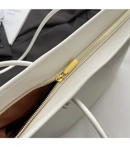 Macro detail of golden metal zipper closure on white leather tote with brown lining