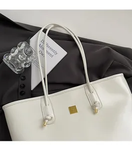 Close-up of white patent leather tote bag with gold metal logo and knotted shoulder strap