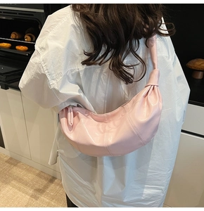 Close-up of light pink croissant bag with glossy finish and knotted strap detail