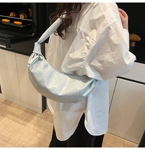 Close-up of light blue glossy crescent bag with ruched design and decorative knot strap