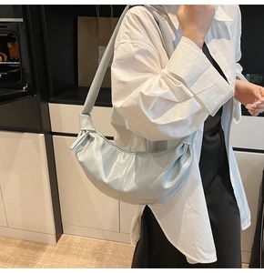 Detail of light blue glossy crescent bag featuring unique pleated texture and smooth zipper