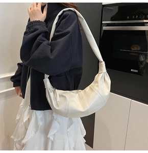 Detail of a beige leather crescent bag featuring chic pleated sides and a stylish top handle