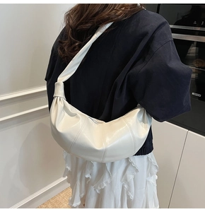 Detail of white glossy crescent bag with stitching and decorative knot strap on model