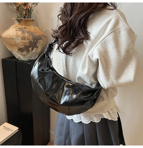 Detail of glossy black crescent shoulder bag with vertical quilting on smooth leather