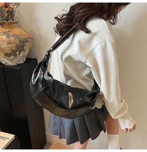 Detail of black glossy half-moon bag featuring unique knotted strap and stitched leather