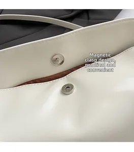 Detail of the magnetic snap closure and brown fabric lining on a white leather handbag