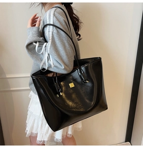 Side view of large black glossy tote bag with gold logo on a model for daily commute