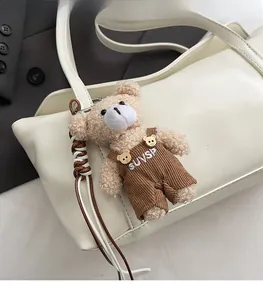 Detail of white leather tote bag featuring a cute brown plush bear charm and clear texture