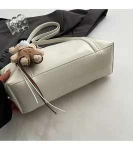 Detail of cream leather bowling bag with plush bear charm and side logo lettering