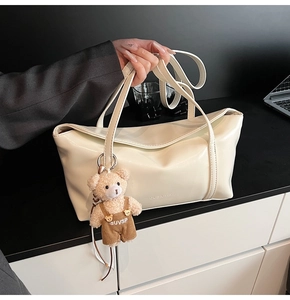 Detail showing cream white leather tote bag with a cute brown teddy bear plush charm