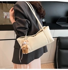 Detail of cream leather shoulder bag featuring an embossed logo and a cute bear pendant