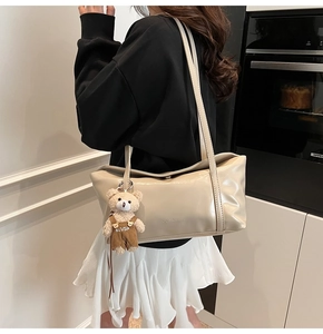 Detail of cream tote bag featuring shiny faux leather texture and a cute teddy bear charm
