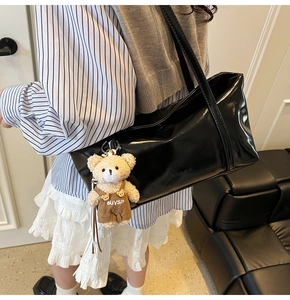 Detail of glossy black shoulder bag with cute teddy bear charm and metallic shine