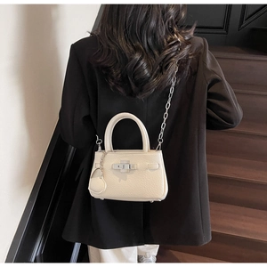 Close-up of mini bucket bag in beige lychee leather with metal twist lock and heart charm