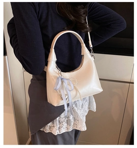 Detail of a creamy white crescent handbag with pearl chain and blue plaid bow accessory
