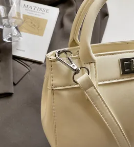 Detail shot of silver metal hardware and fine stitching on a beige leather handbag