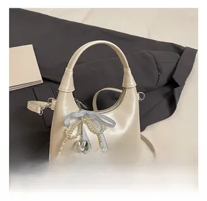 Detail of cream crescent bag with blue bow, pearl chains, and silver heart charm
