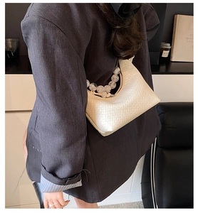 Détail du sac baguette blanc cassé avec motif crocodile et anse perlée élégante