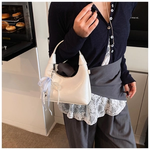 Détail d'un sac demi-lune blanc avec ruban à carreaux bleus et breloque noeud en perles