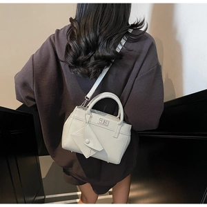 Detail view of a light gray crossbody bag with a metal twist lock and decorative mini pouch