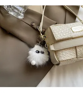 Detail der geflochtenen Handtasche mit weißem Monster-Anhänger auf braunem Blazer-Hintergrund