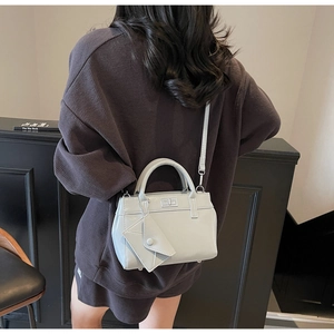 Model wearing a light gray trapezoid handbag with a metal lock and adjustable strap