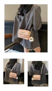 Detail einer rosa Handtasche mit Webstruktur, Goldplakette und flauschigem Anhänger
