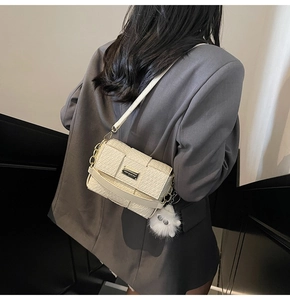 Detail der cremeweißen Handtasche mit Krokodilmuster und flauschigem Anhänger