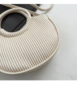 Close-up of cream crescent handbag featuring fine vertical pleated texture and slim strap