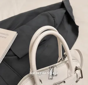 Close-up of litchi-pattern cream shell bag with silver zipper and dual handles