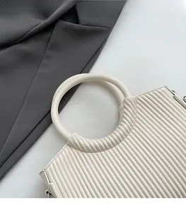 Detail of minimalist cream bucket bag with vertical pleats and round metal handle