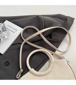 Detail of off-white pleated handbag showing circular handle and adjustable shoulder strap