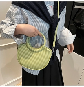 Vertical pleated lime green crescent handbag with a ring handle worn by a model