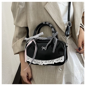 Detail of black patent leather Boston bag with metal bow and lace trim decoration