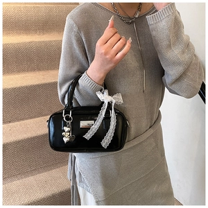 Detail of black patent handbag with white lace bow and heart charms on model