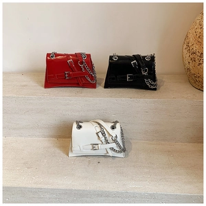 Three patent leather crossbody bags in red, black, and white with chain straps on steps