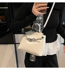 Detail of white PU leather crossbody bag with chain and bow decoration on the model