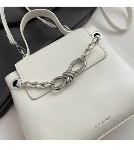 Close-up of white leather handbag featuring a shiny silver knotted chain decoration