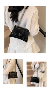 Détail d'un sac bandoulière noir brillant avec chaîne argentée et boucles décoratives