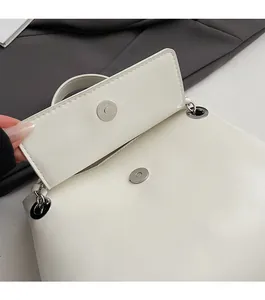 Detail of the silver magnetic closure on a white leather shoulder bag with logo branding
