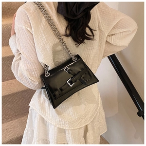 Detail of a chic black crossbody bag with silver chains and buckles on a white dress
