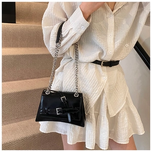 Chic black glossy shoulder bag with dual metal buckles and silver chain on model