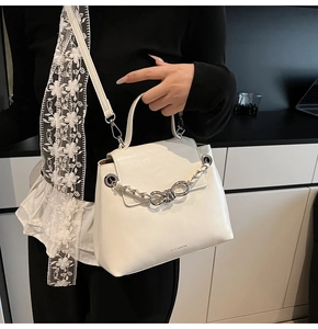 Close-up of a white leather crossbody bag featuring a thick metal knot chain and logo