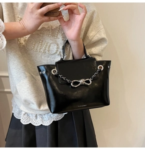 Detail of black glossy handbag featuring silver chain, bow buckle, and metal rings