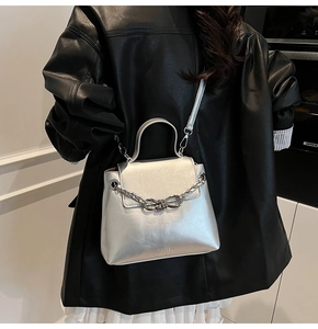 Detail of silver metallic handbag featuring bow-knot chain and sleek buckle closure