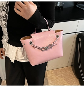 Pink glossy leather crossbody bag with metallic chain detail shown on a model
