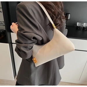 Detailansicht der cremefarbenen Halbmond-Tasche mit goldenem Metallanhänger für Damen